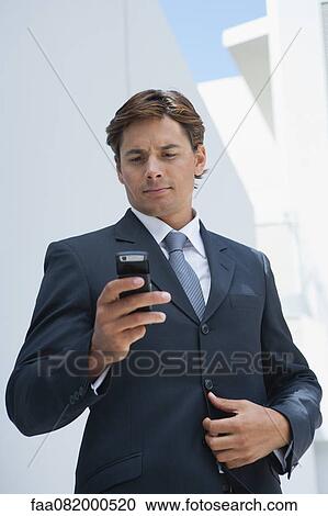 Stock Image - Businessman text messaging with cell phone. Fotosearch