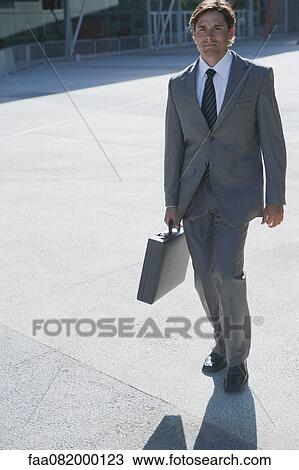 Businessman walking outdoors with briefcase in hand View Large Photo Image Stock Image - Businessman walking outdoors with briefcase in hand. Fotosearch