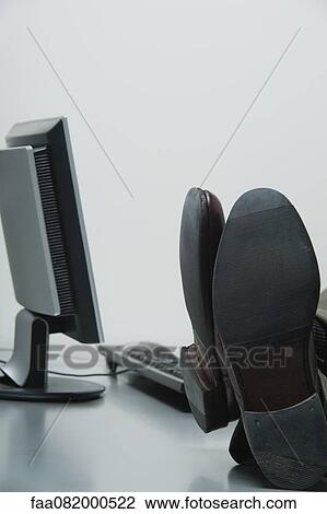 Stock Image - Businessman with feet up on desk in office, cropped. Fotosearch