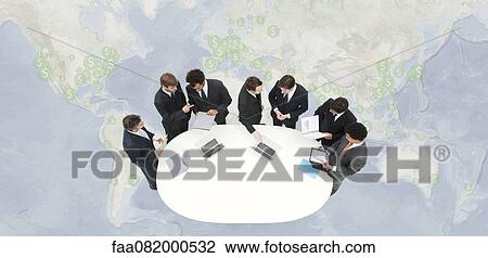 Stock Image - Businessmen in meeting, standing on world map marked with dollar signs. Fotosearch