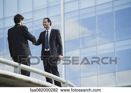 Stock Image - Businessmen shaking hands outdoors. Fotosearch