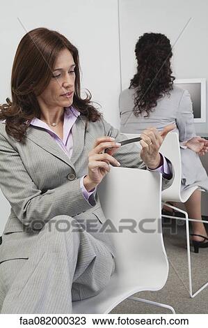 Stock Image - Businesswoman filing her nails at work. Fotosearch