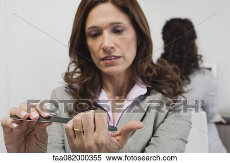 Businesswoman filing her nails at work View Large Photo Image Stock Photography - Businesswoman filing her nails at work. Fotosearch