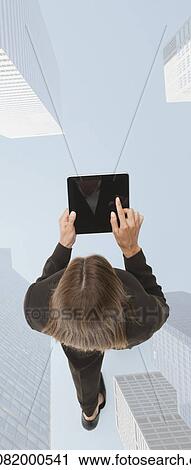 Stock Image - Businesswoman using digital tablet while walking on superimposed image of skyscrapers. Fotosearch