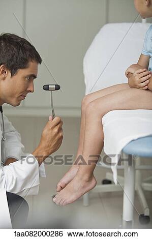 Stock Photograph - Doctor checking boy's reflexes with reflex hammer, side view, cropped. Fotosearch