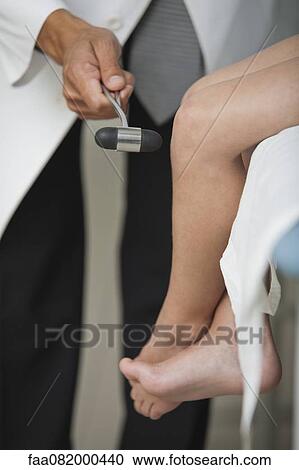 Stock Image - Doctor checking child's reflexes with reflex hammer, cropped. Fotosearch