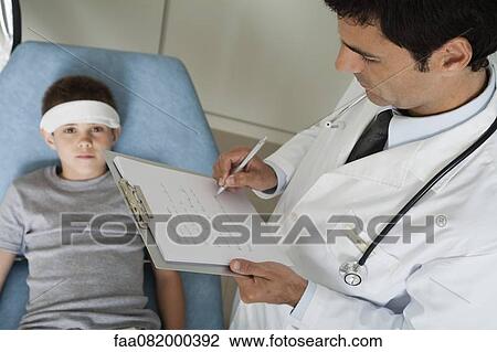 Stock Image - Doctor monitoring young patient with bandage on his head. Fotosearch