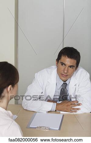 Doctor sitting across from female patient View Large Photo Image Stock Photograph - Doctor sitting across from female patient. Fotosearch