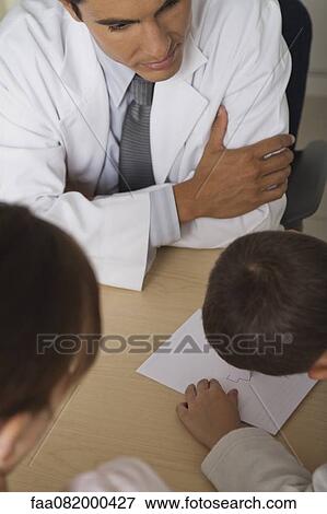 Stock Photo - Doctor sitting with boy and woman, boy drawing on paper. Fotosearch