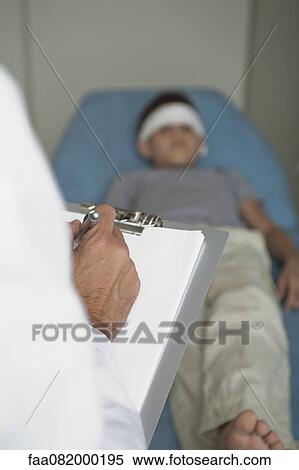 Doctor writing on clipboard, boy lying on examination table with bandage on forehead in background View Large Photo Image Stock Photography - Doctor writing on clipboard, boy lying on examination table with bandage on forehead in background. Fotosearch