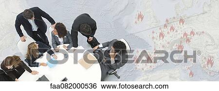 Stock Photograph - Executives in meeting, large map depicting European economic crisis in background. Fotosearch