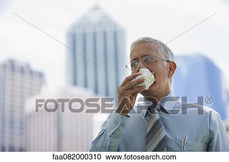Stock Image - Mature businessman eating lunch while walking outdoors. Fotosearch
