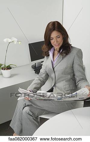 Stock Photo - Mature businesswoman reading newspaper in office. Fotosearch