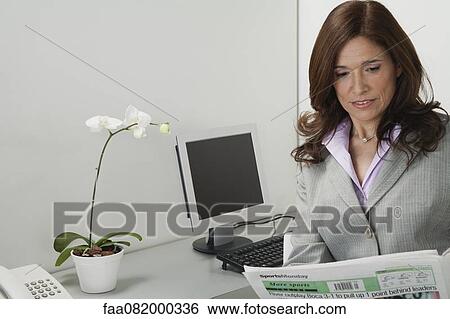 Stock Photograph - Mature businesswoman reading newspaper in office. Fotosearch
