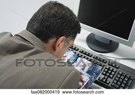 Stock Photo - Mature man reading comic book at desk in office, rear view. Fotosearch
