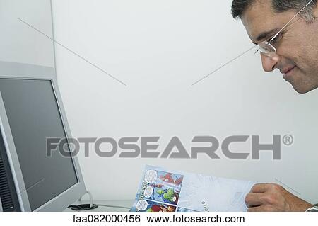 Stock Photograph - Mature man reading comic book in office. Fotosearch