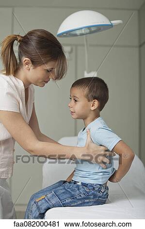 Stock Image - Mother helping little boy on examination table. Fotosearch