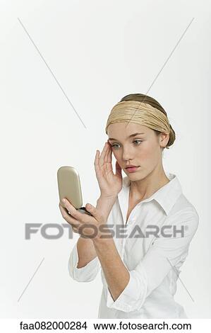 Picture - Preteen girl looking at herself in mirror compact. Fotosearch