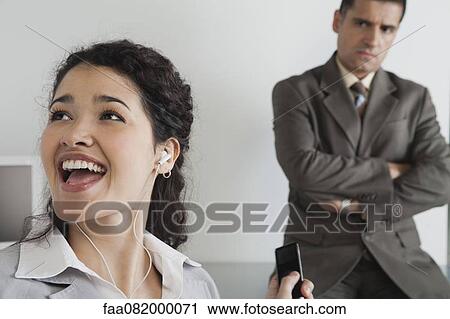 Woman distractedly listening to MP3 player at work, boss glaring in background View Large Photo Image Stock Image - Woman distractedly listening to MP3 player at work, boss glaring in background. Fotosearch