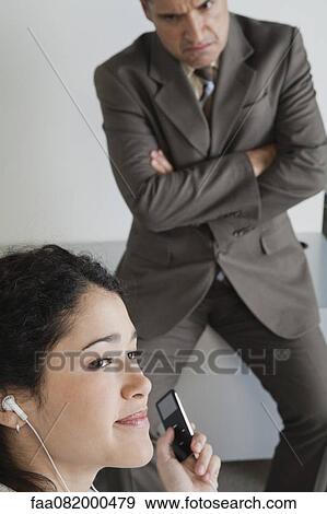 Woman distractedly listening to MP3 player at work, angry boss in background View Large Photo Image Stock Photo - Woman distractedly listening to MP3 player at work, angry boss in background. Fotosearch