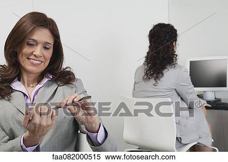 Stock Photography - Woman filing her nails in office, colleague working in background. Fotosearch
