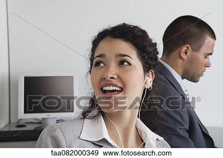 Stock Photo - Woman listening to earphones and daydreaming in office. Fotosearch