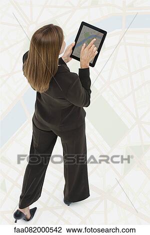 Stock Image - Woman looking at map on digital tablet while walking on large map. Fotosearch