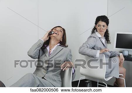 Woman looking over shoulder at coworker laughing on cell phone in office View Large Photo Image Stock Photograph - Woman looking over shoulder at coworker laughing on cell phone in office. Fotosearch