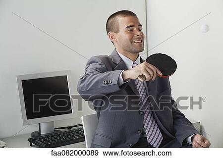 Stock Photo - Young man playing table tennis in office. Fotosearch