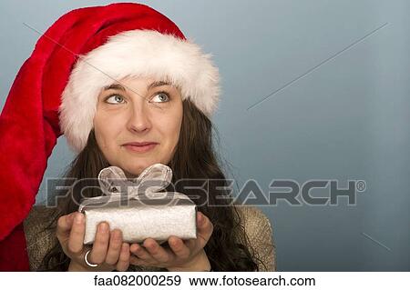 Young woman holding Christmas present, looking up in thought View Large Photo Image Stock Photo - Young woman holding Christmas present, looking up in thought. Fotosearch