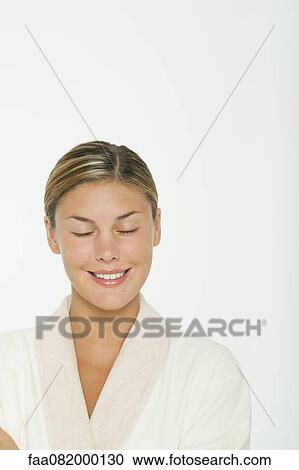 Stock Image - Young woman in bathrobe, smiling with eyes closed. Fotosearch