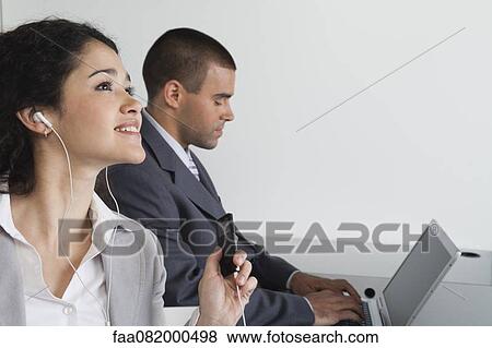 Stock Photo - Young woman listening to MP3 player in office. Fotosearch