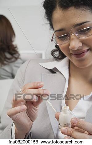 Young woman painting her fingernails at work View Large Photo Image Stock Photo - Young woman painting her fingernails at work. Fotosearch