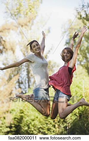 Young women jumping in air, smiling View Large Photo Image Stock Image - Young women jumping in air, smiling. Fotosearch