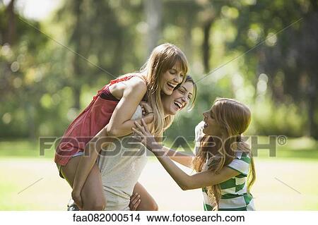 Picture - Young women playing, one woman giving another piggyback ride. Fotosearch