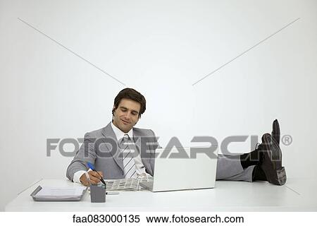 Stock Photography - Businessman sitting with feet on desk, looking at newspaper. Fotosearch
