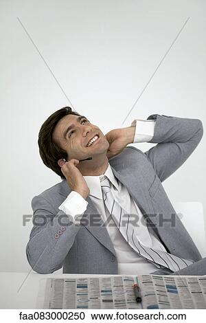 Businessman sitting with newspaper, talking on headset View Large Photo Image Stock Image - Businessman sitting with newspaper, talking on headset. Fotosearch