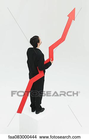 Picture - Businessman standing at top of steps holding arrow pointed upward. Fotosearch