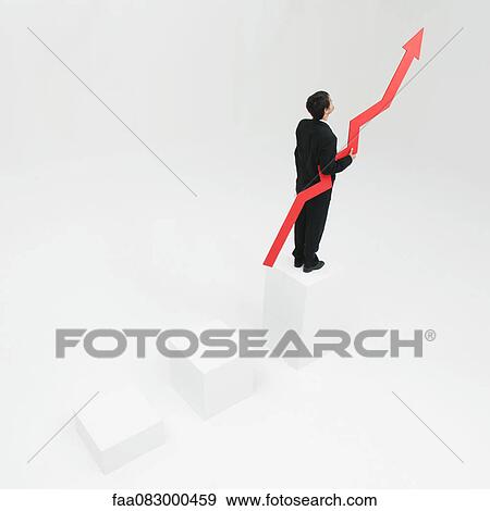 Stock Photo - Businessman standing at top of steps holding arrow pointed upward. Fotosearch