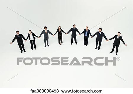 Stock Image - Businessmen and businesswomen standing together holding hands. Fotosearch