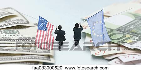 Stock Image - Businessmen marching between piles of money, carrying American and European Union flags. Fotosearch