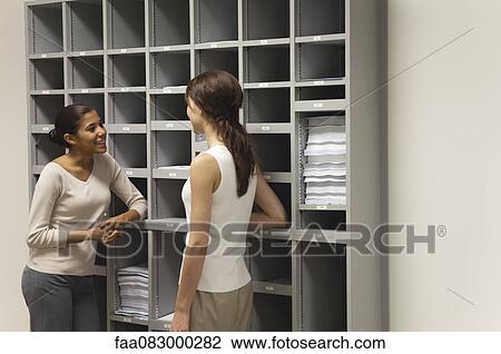 Colleagues chatting in front of filing shelves in office View Large Photo Image Stock Image - Colleagues chatting in front of filing shelves in office. Fotosearch