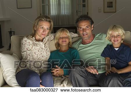 Stock Photo - Family sitting together on sofa, watching TV. Fotosearch