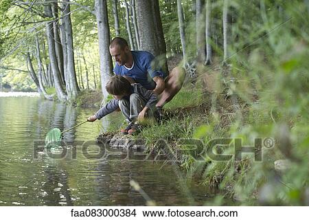 Father and son crouching at water's edge with fishing net View Large Photo Image Picture - Father and son crouching at water's edge with fishing net. Fotosearch