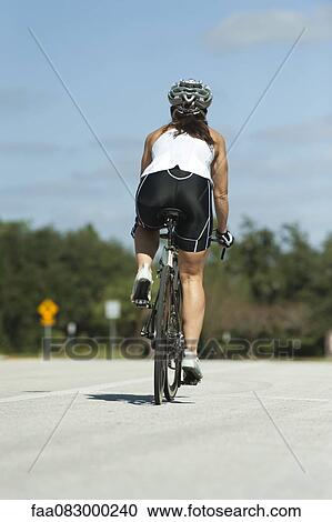 Female cyclist cycling on road View Large Photo Image Stock Image - Female cyclist cycling on road. Fotosearch
