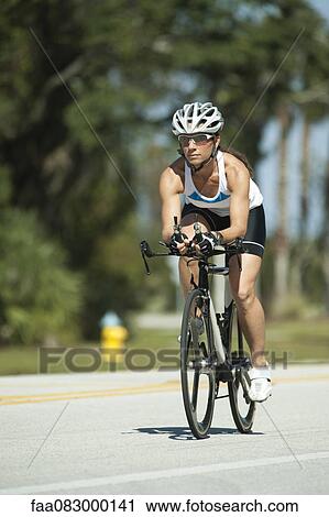 Stock Image - Female cyclist riding on road. Fotosearch