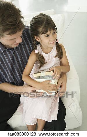 Little girl sitting on father's laps opening present View Large Photo Image Stock Photo - Little girl sitting on father's laps opening present. Fotosearch