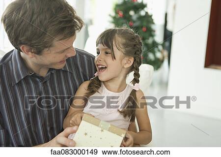 Stock Photo - Little girl sitting on father's laps holding present. Fotosearch