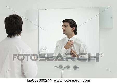Picture - Man adjusting shirt collar in mirror. Fotosearch