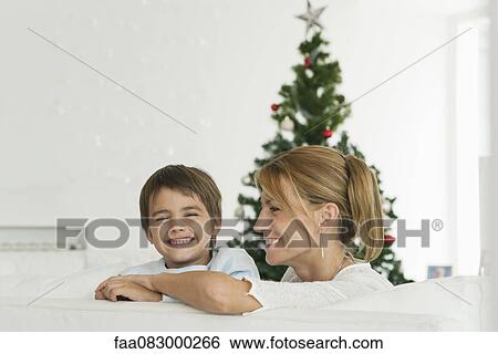Stock Photograph - Mother and son sitting in couch in front of Christmas tree. Fotosearch